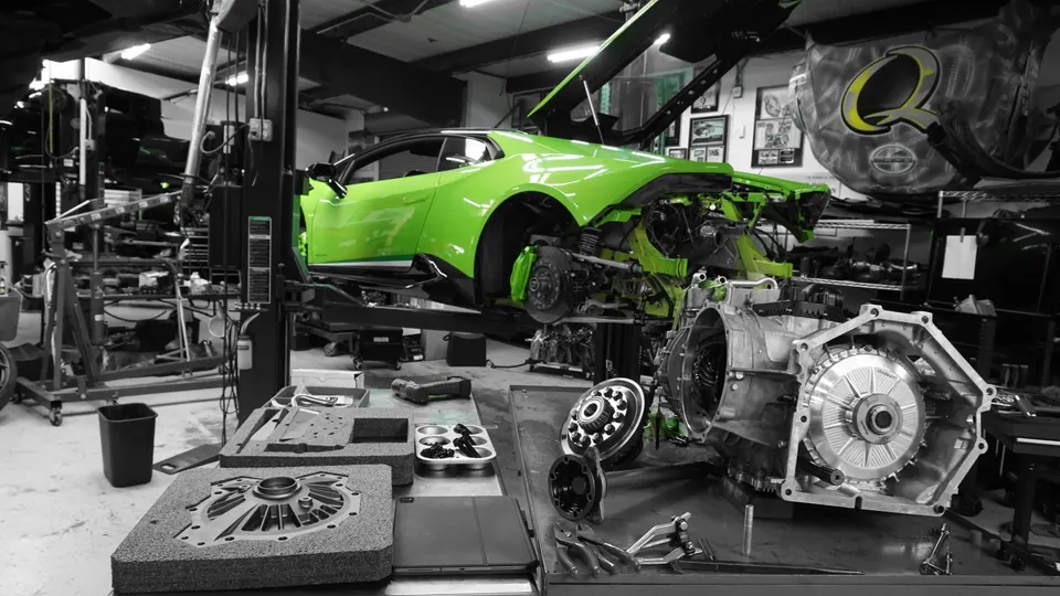 A green Lamborghini Huracan on a lift in a shop with its transmission and other drivetrain components disassembled on a workbench.