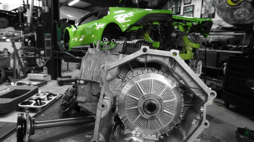 A green Lamborghini Huracan on a lift in a performance shop, with a high-performance transmission on a workbench in the foreground.