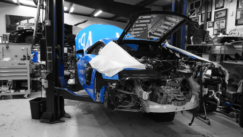 A blue car on a lift in a performance tuning shop, undergoing extensive disassembly and engine work.