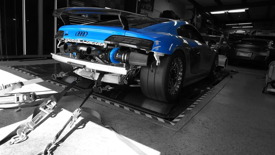 Blue Audi R8 twin-turbo on a dyno at a performance tuning shop, showcasing the exposed turbo system and drag slicks.