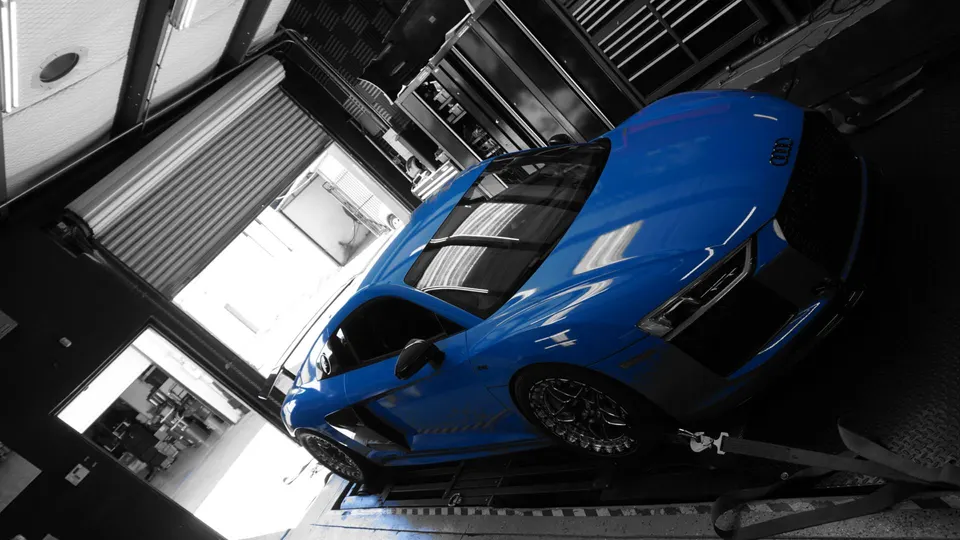 A blue Audi R8 supercar strapped down on a dynamometer at a performance tuning shop, ready for a power run.
