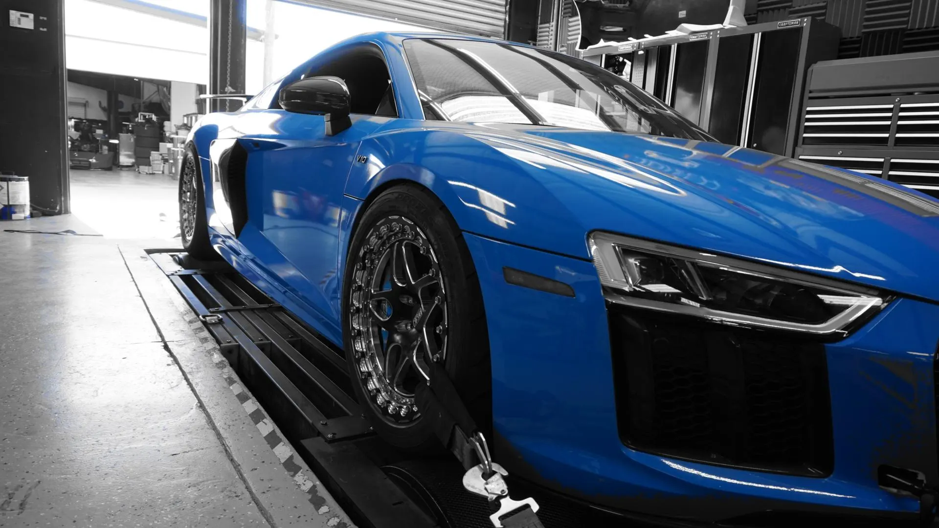 Blue Audi R8 supercar strapped down on a dynamometer for performance testing at a tuning shop.