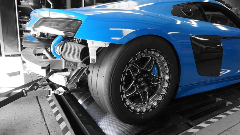A blue Audi R8 with its rear bumper removed, showcasing a large turbocharger and drag slicks, strapped to a dyno.