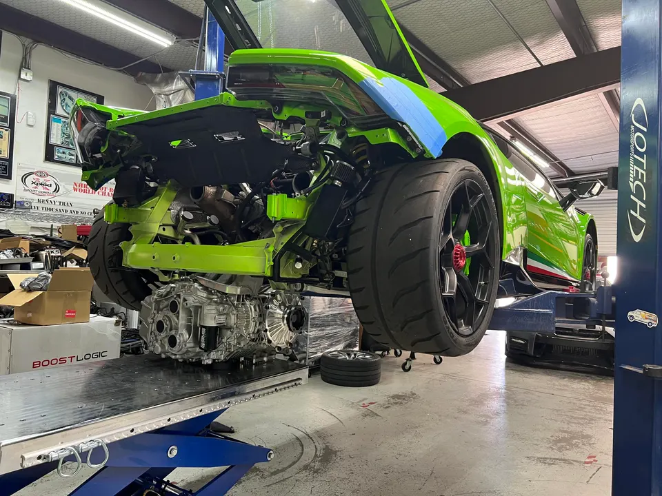A green Lamborghini Huracan on a lift in a performance shop with its engine and drivetrain removed for service.