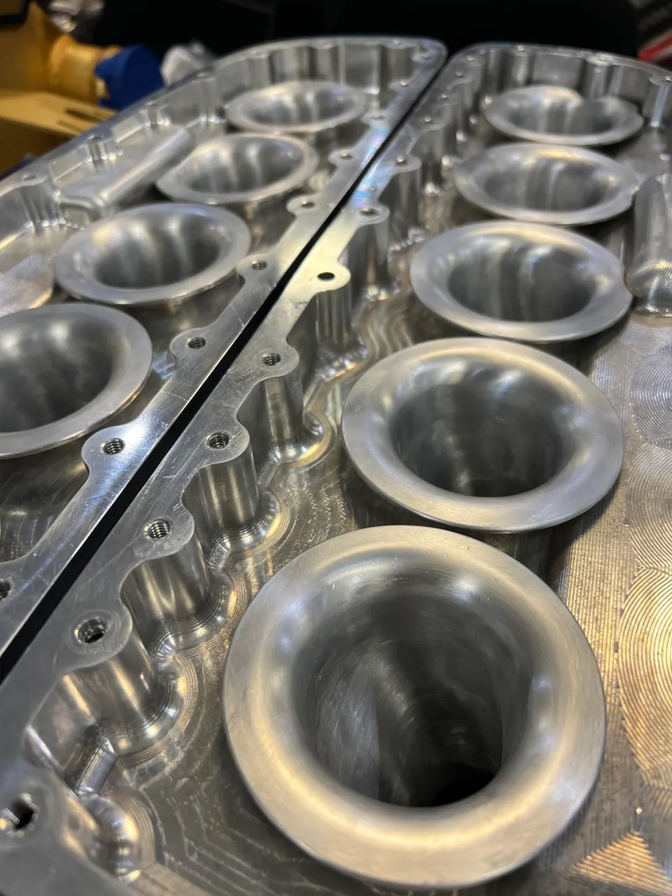 Close-up of a precision machined aluminum intake manifold with velocity stacks for an automotive performance engine.