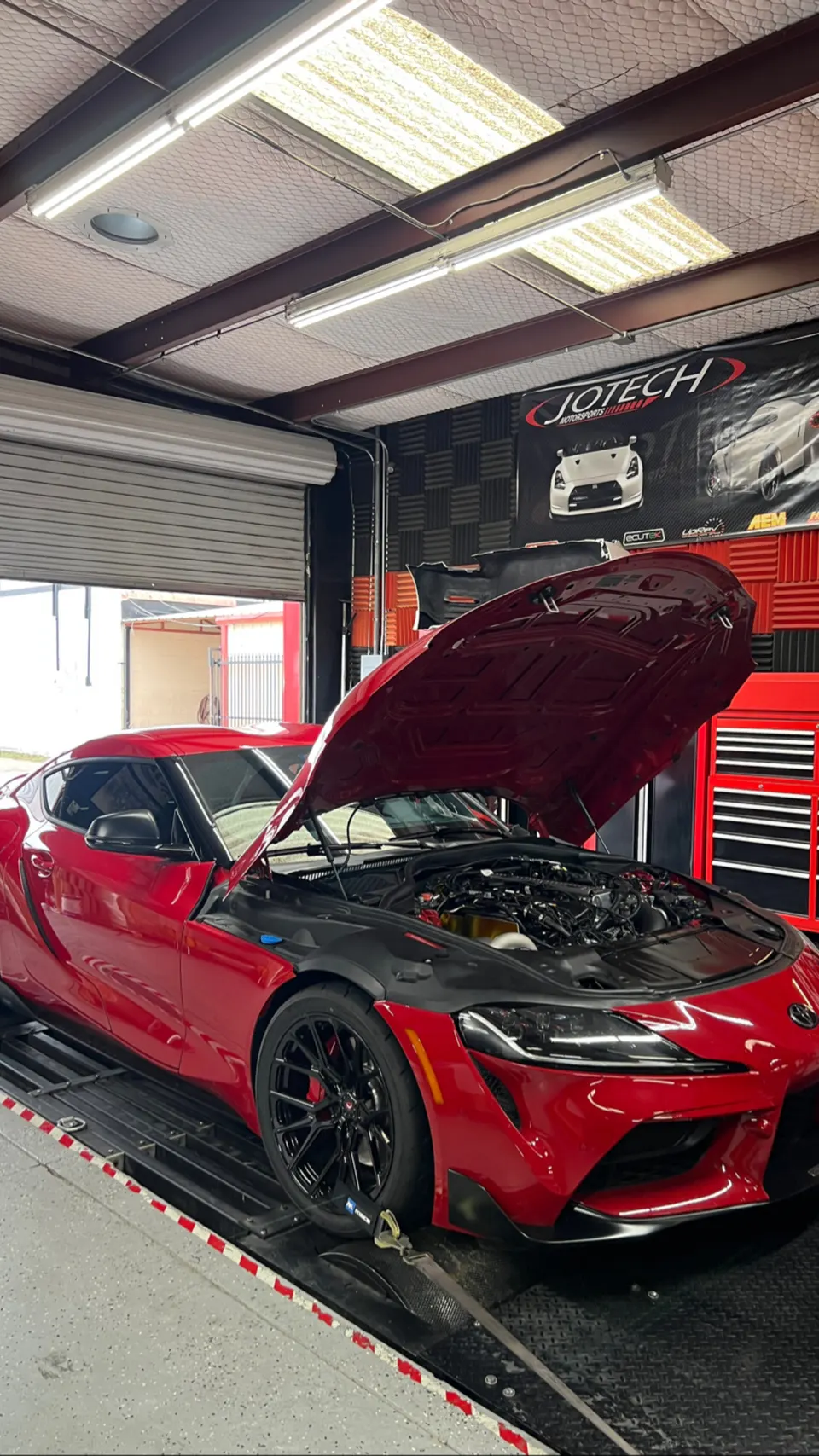 A red Toyota Supra MK5 with its hood open, strapped to a dynamometer at Jotech Motorsports for performance tuning.