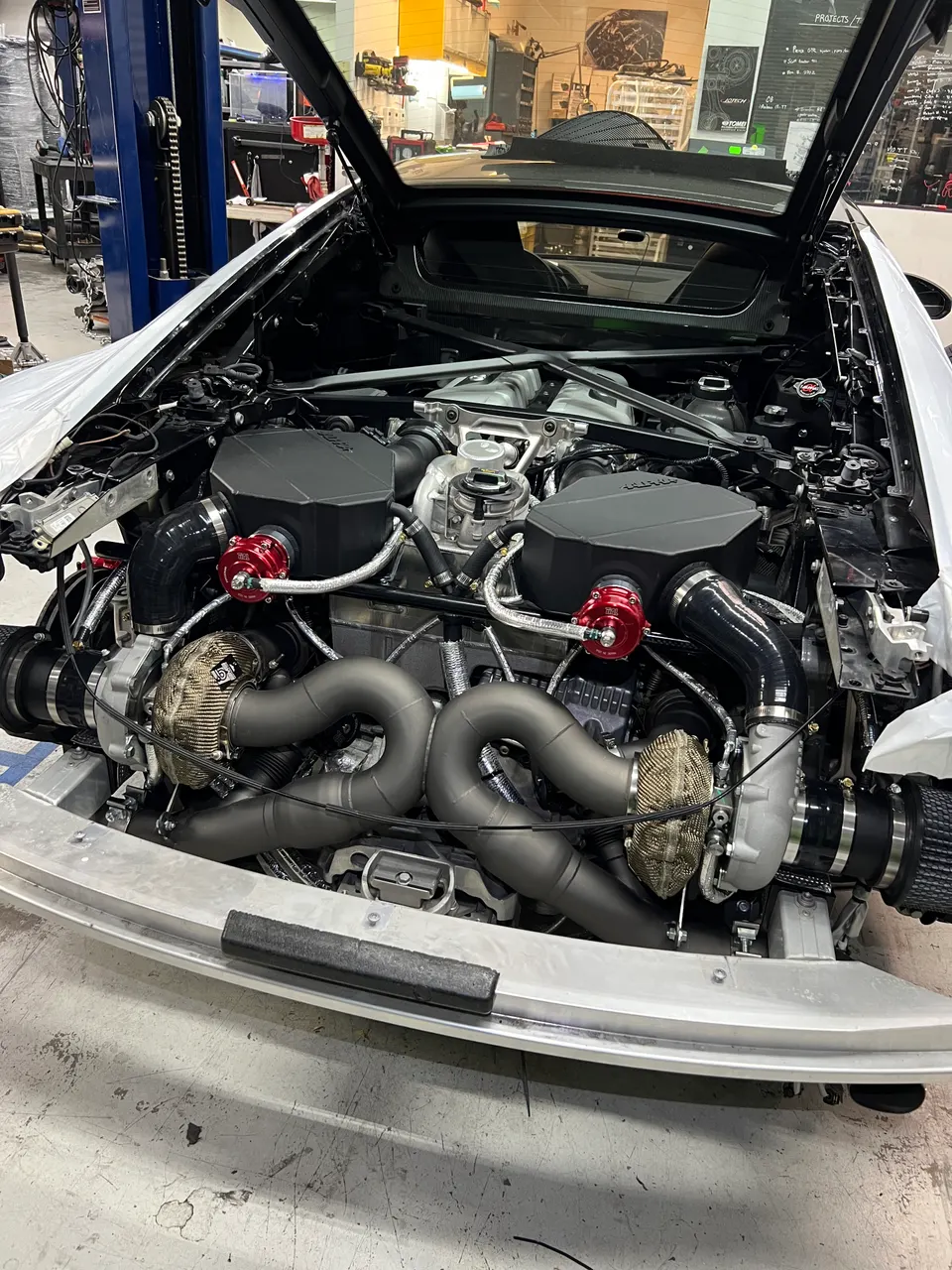 A white Lamborghini Huracan with a twin-turbo engine conversion in a Jotech Motorsports shop, showcasing custom fabrication.