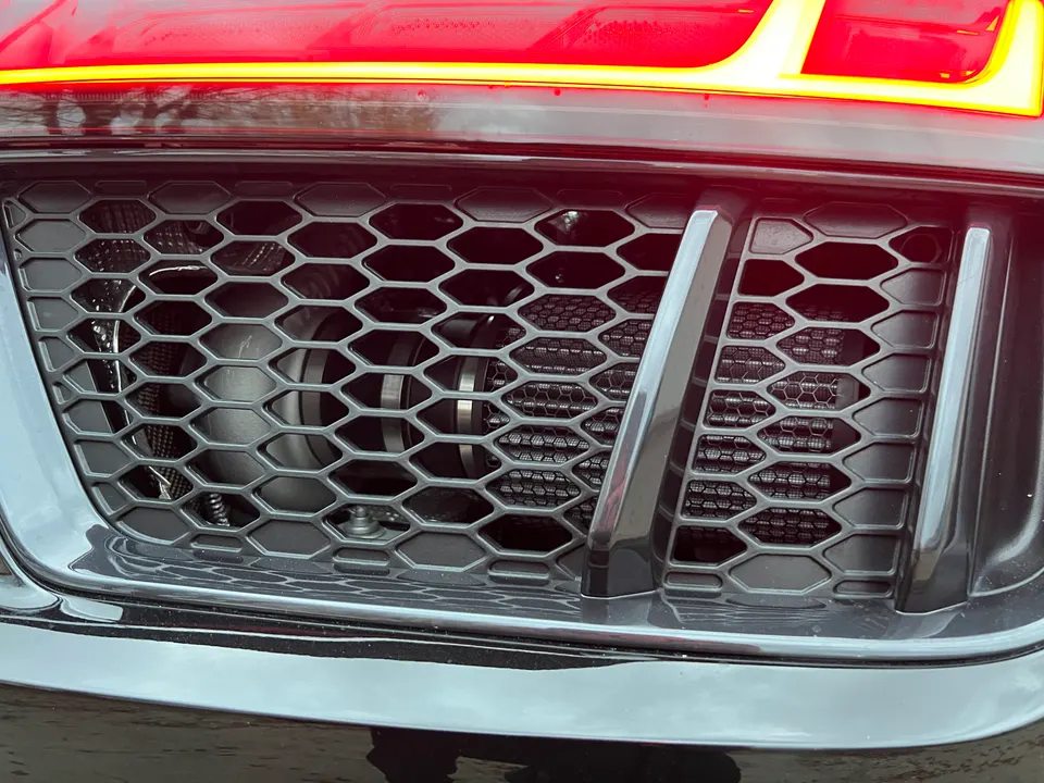A close-up of a car's front grille revealing a performance intercooler and turbocharger behind the honeycomb mesh.