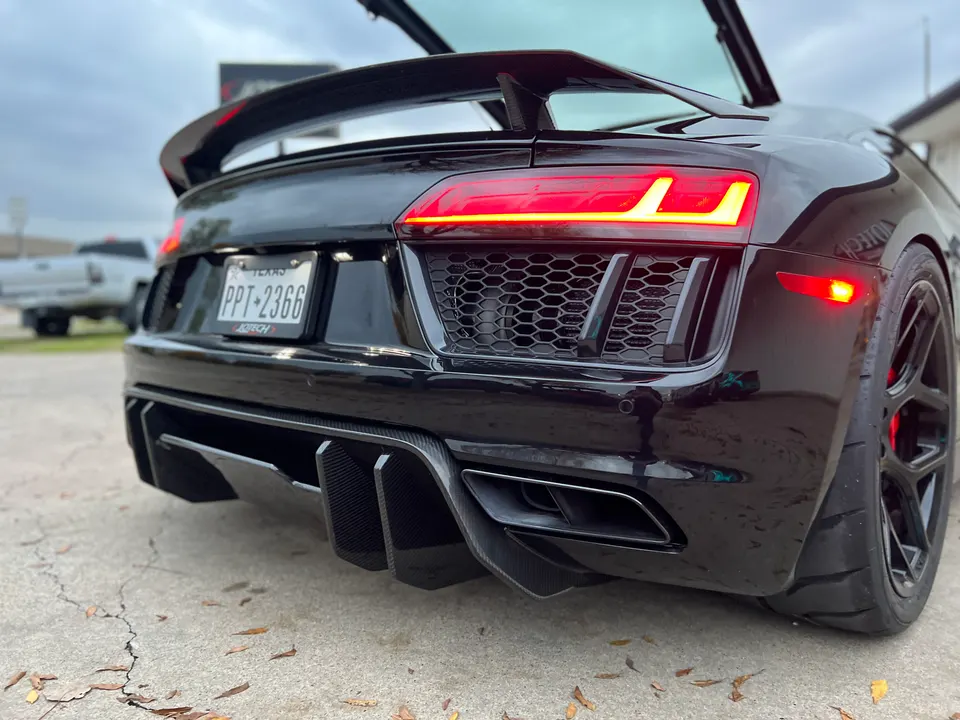 Rear view of a black Audi R8 with a carbon fiber diffuser and rear wing, showcasing its aggressive styling.