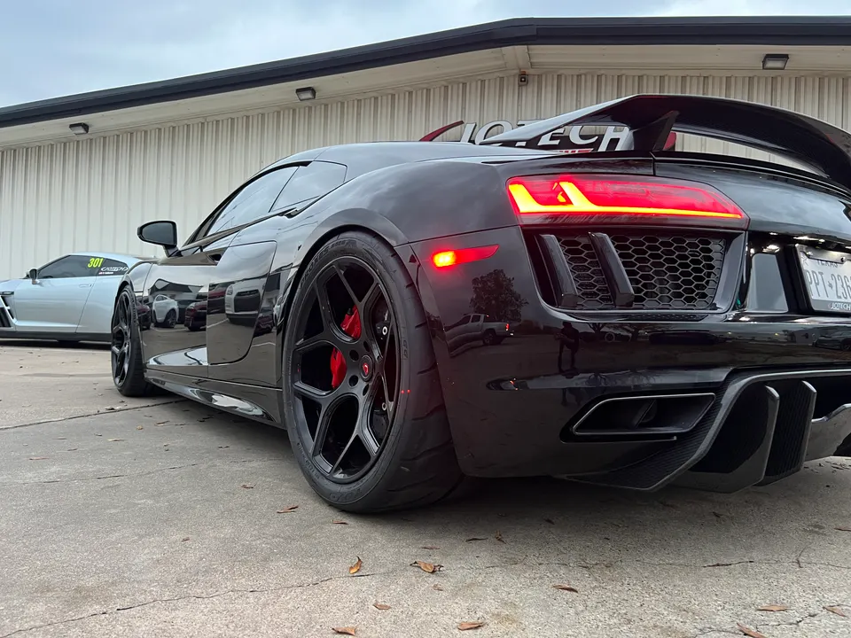 Black Audi R8 with aftermarket wheels, red brake calipers, and a large rear wing parked outside Jotech Motorsports.