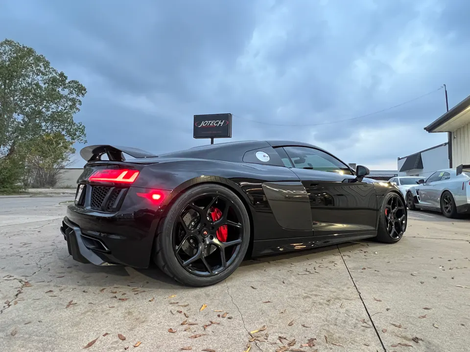 Black Audi R8 with aftermarket wheels, red brake calipers, and a carbon fiber rear wing parked outside Jotech Motorsports.