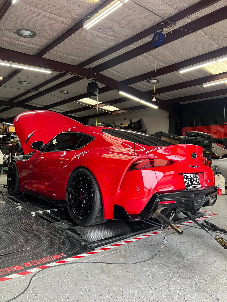 Red Toyota Supra on a dyno at Jotech Motorsports, undergoing performance tuning and exhaust testing.
