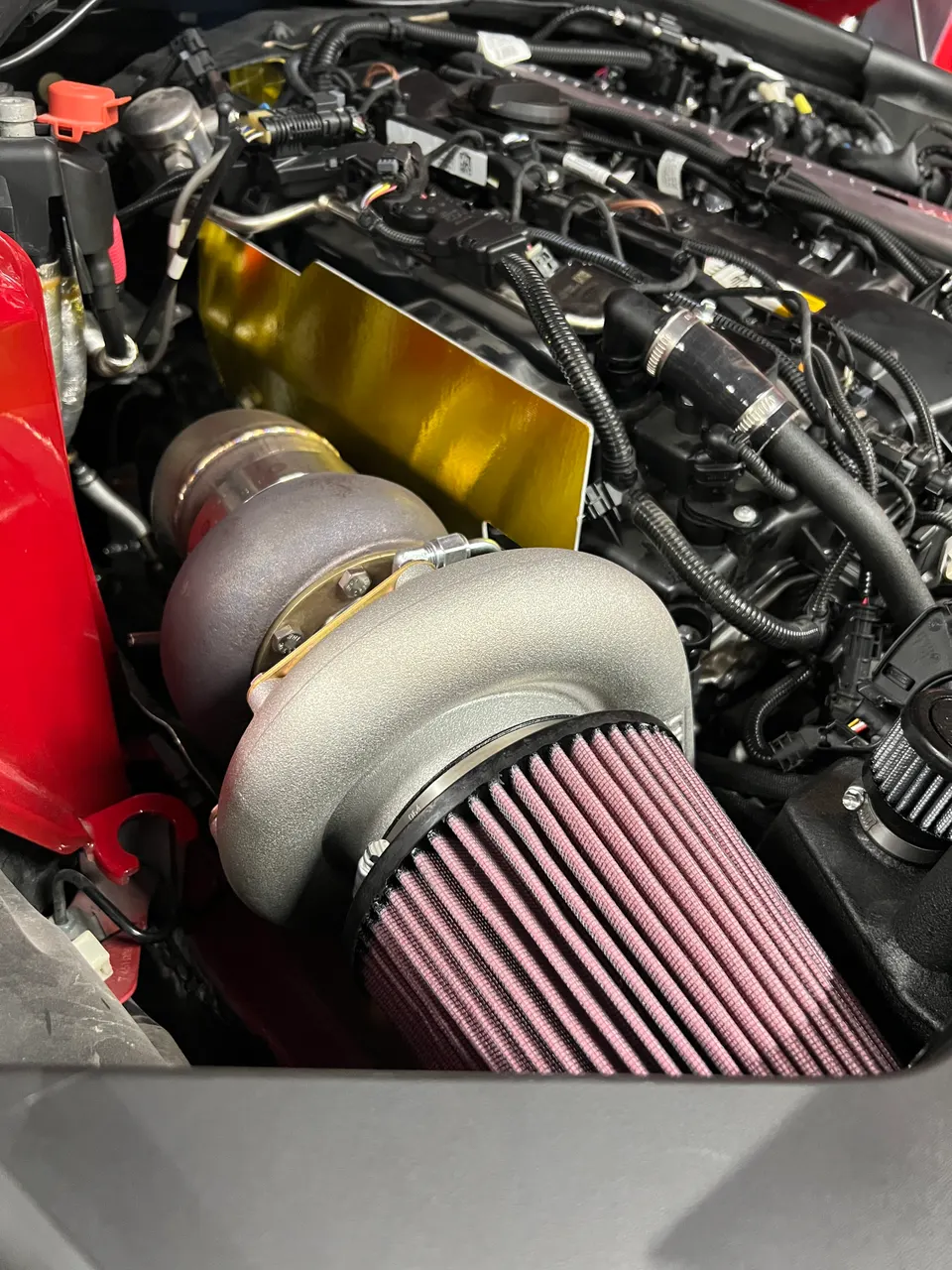 Close-up of a high-performance engine bay featuring a large aftermarket turbocharger and a conical air filter with a gold heat shield.