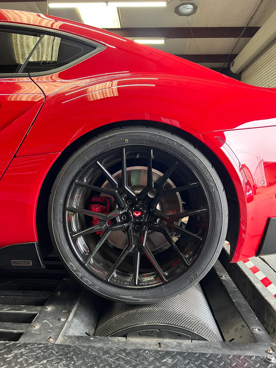 A red Toyota Supra on a dyno, showcasing Vossen wheels, Toyo tires, and red brake calipers.