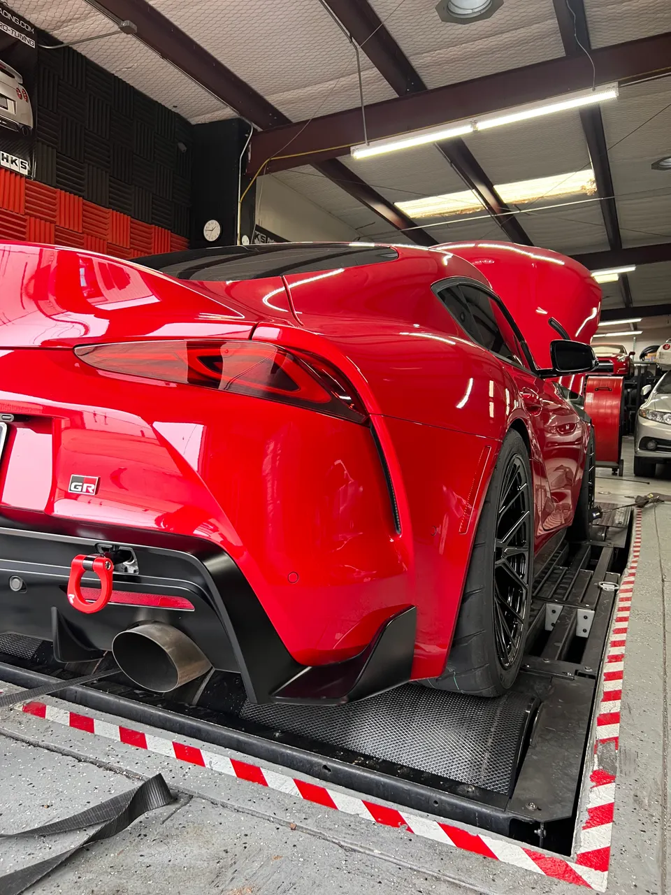 Red Toyota GR Supra on a dyno at a performance tuning shop, showcasing its rear and aftermarket exhaust system.
