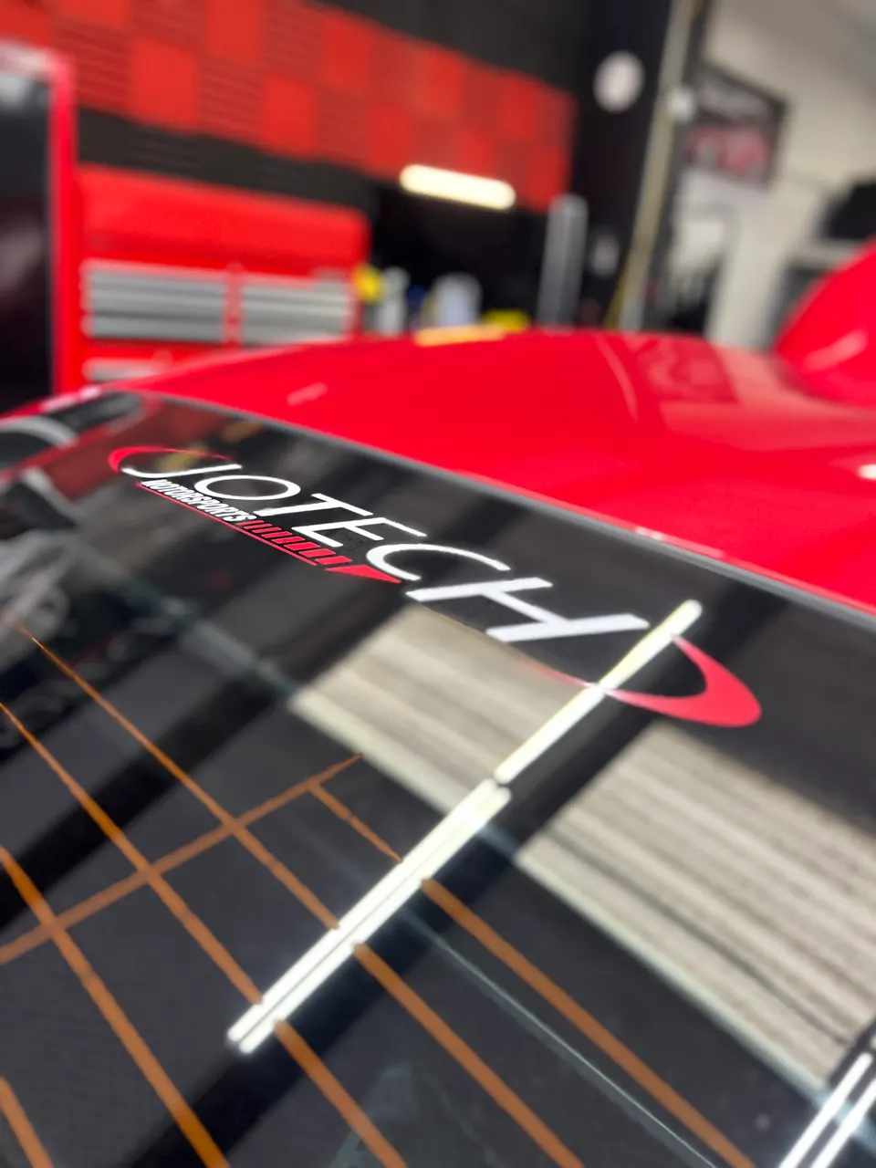 Close-up of a Jotech Motorsports decal on the rear window of a red performance car in a shop environment.