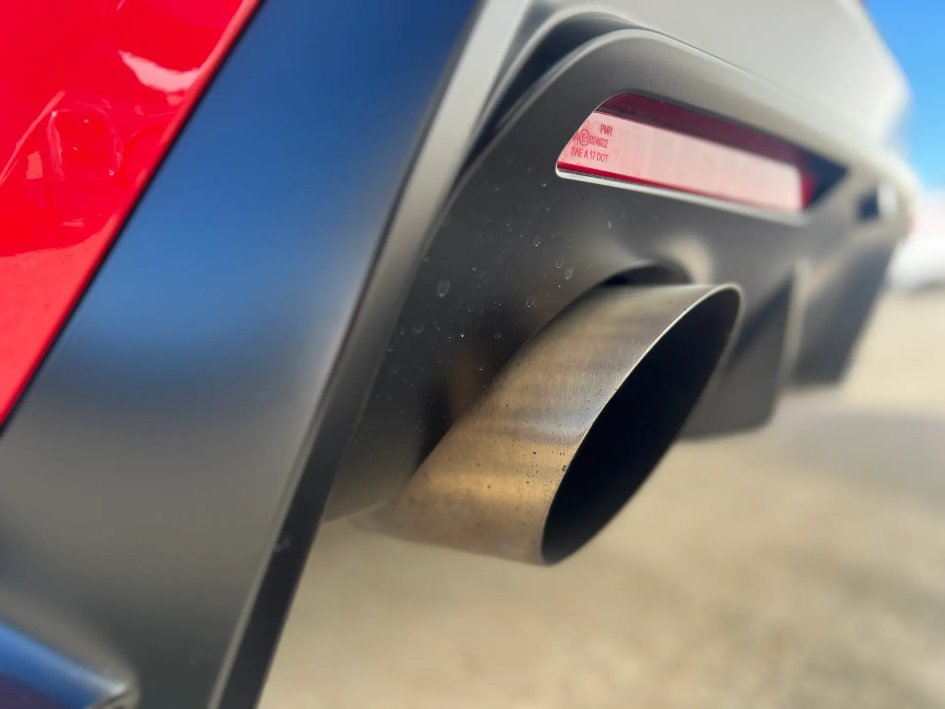 Close-up shot of a car's exhaust tip and rear diffuser, with red bodywork visible.