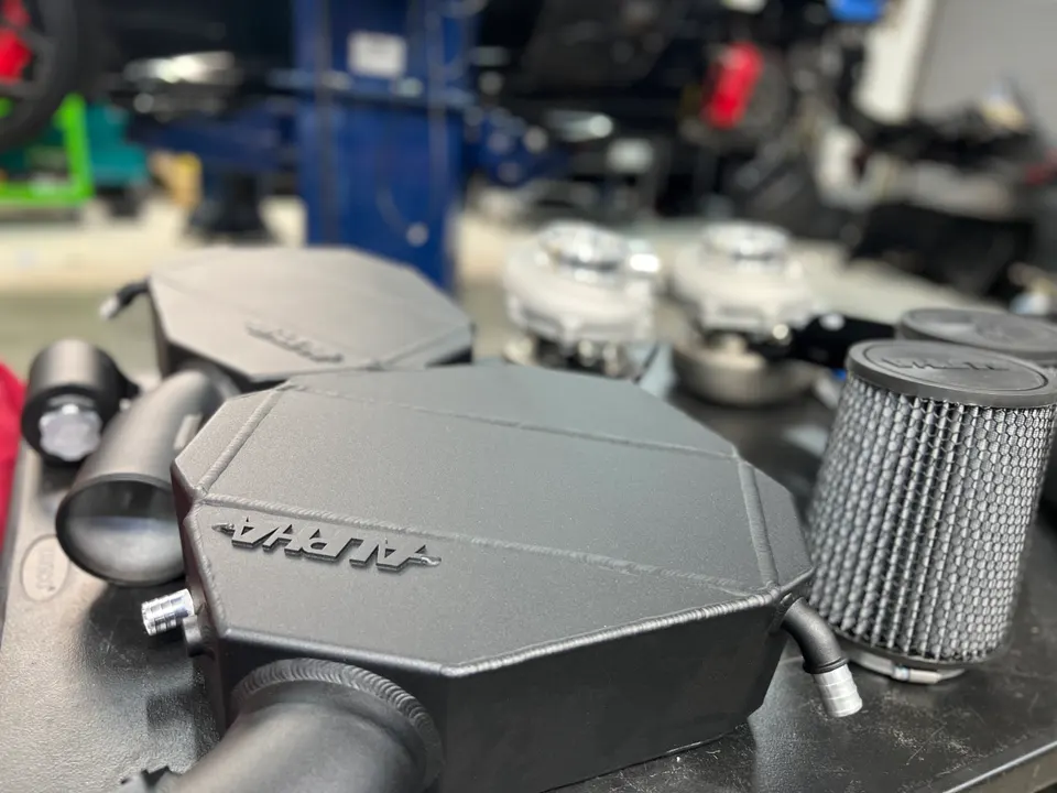Alpha Performance intercoolers, air filters, and and boost piping laid out on a workbench in a performance shop.