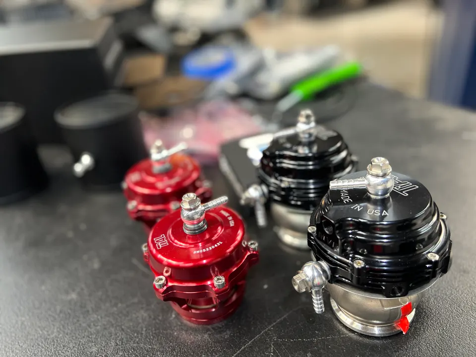 Multiple black and red Tial blow-off valves on a shop bench, ready for installation on a performance vehicle.