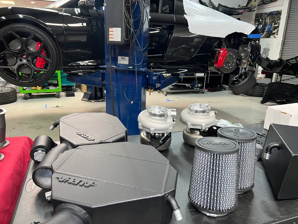 Alfa Romeo Giulia on a lift in a performance shop with turbochargers and air filters on a workbench, ready for install.
