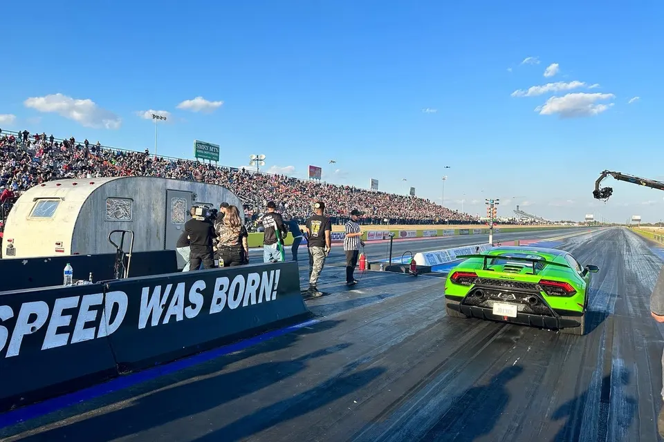 A vibrant green Lamborghini Huracan on a drag strip, with a large crowd in the stands and camera crew nearby.