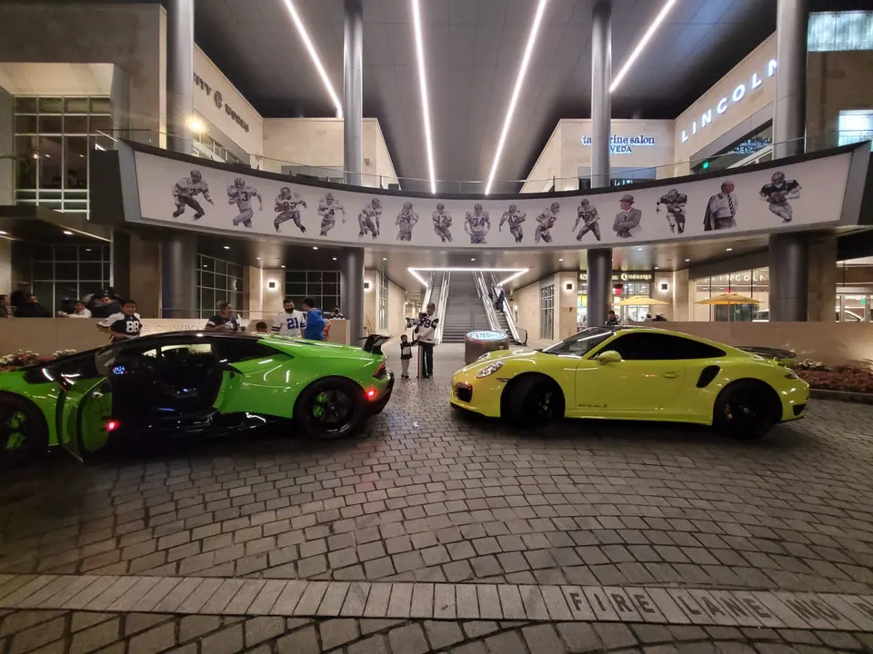 Green Lamborghini Huracan and yellow Porsche 911 Turbo S parked at night in an urban shopping center.