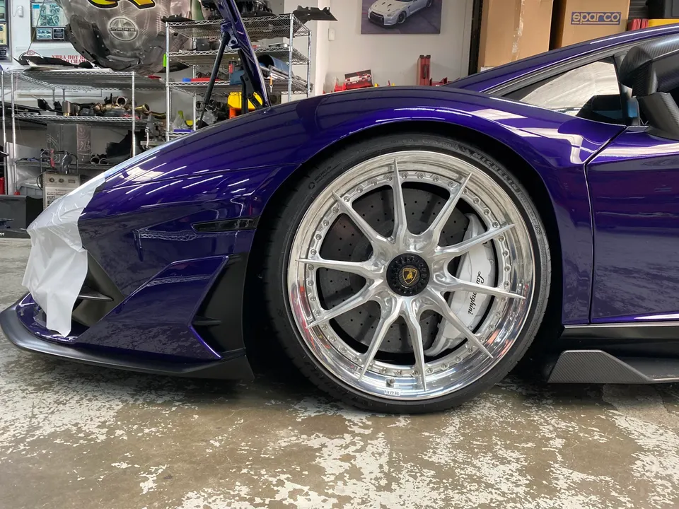 A purple Lamborghini with custom aftermarket multi-spoke wheels and large brakes in a shop setting.