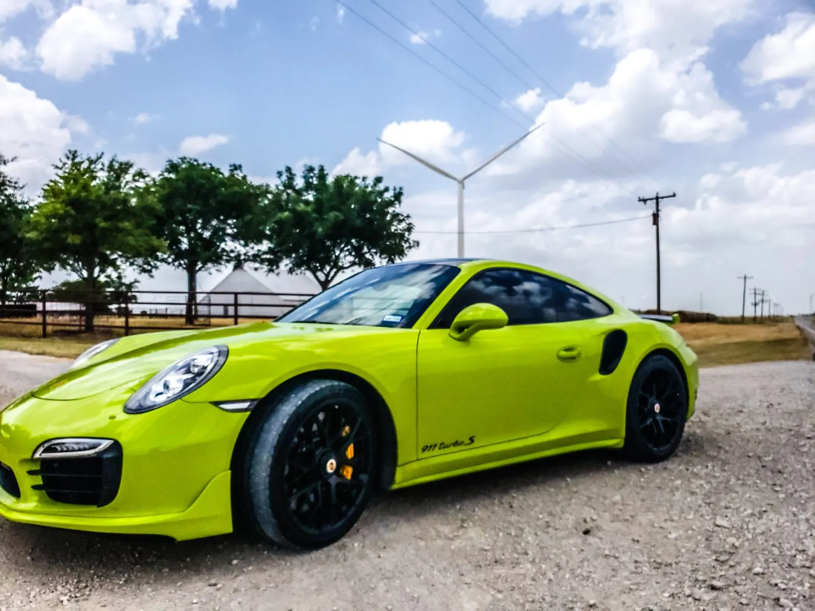 Lime green Porsche 911 Turbo S parked on a gravel road with a wind turbine in the background.
