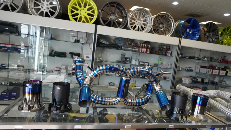 A blue and silver aftermarket exhaust system displayed in a performance tuning shop with various wheels on a shelf.