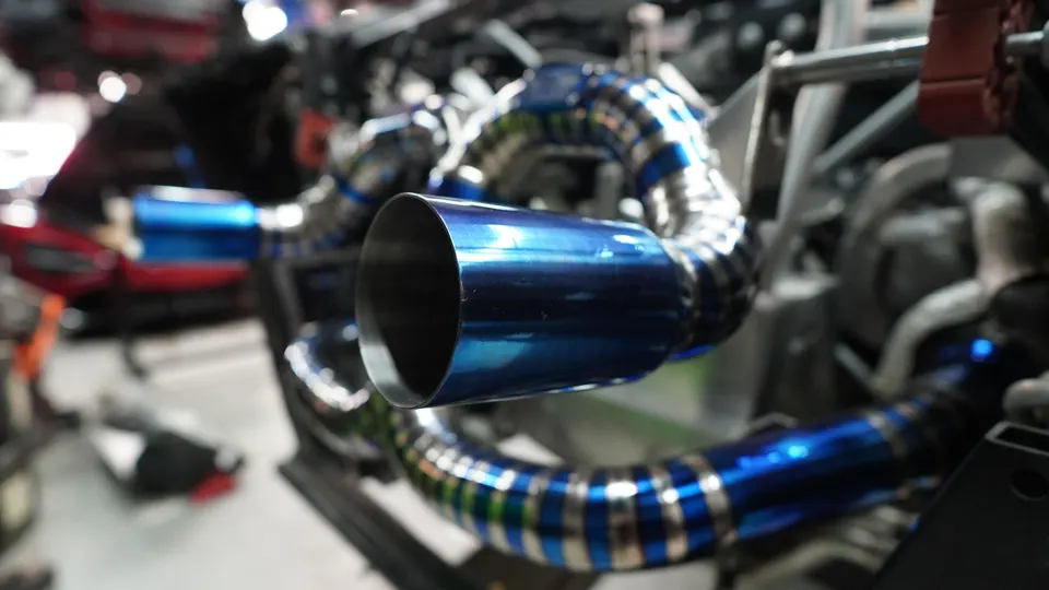Close-up of a vibrant blue titanium performance exhaust system and tip installed on a high-performance car.
