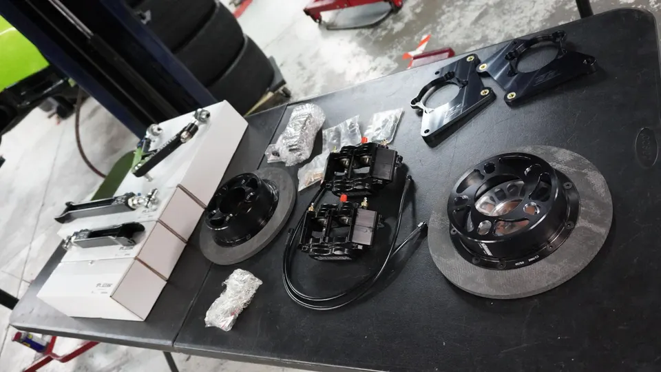 Performance brake rotors, calipers, and suspension components laid out on a table in a tuning shop.