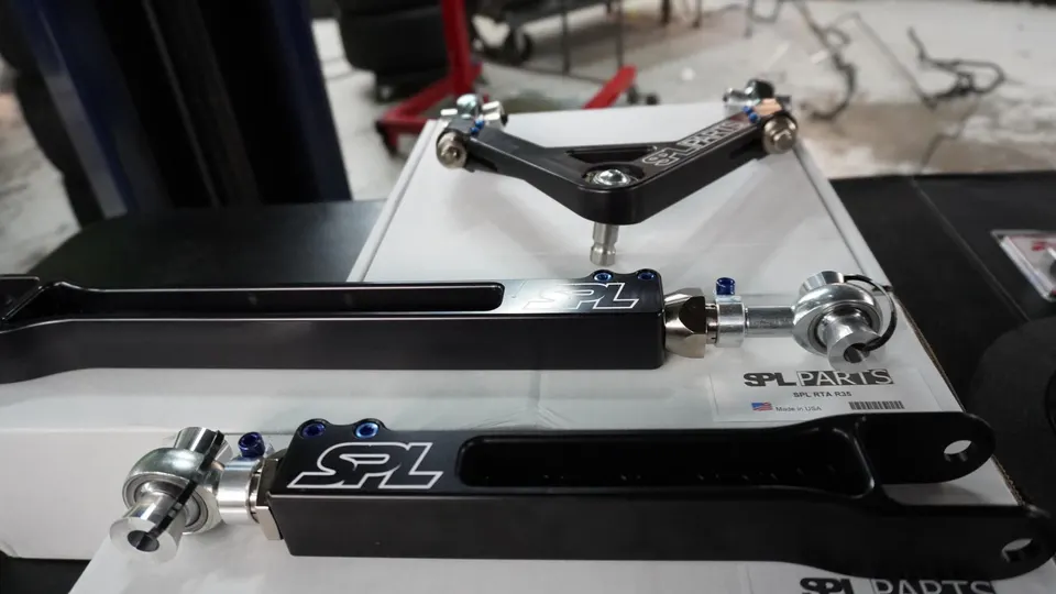 SPL Parts adjustable suspension control arms and links on a workbench in a performance shop