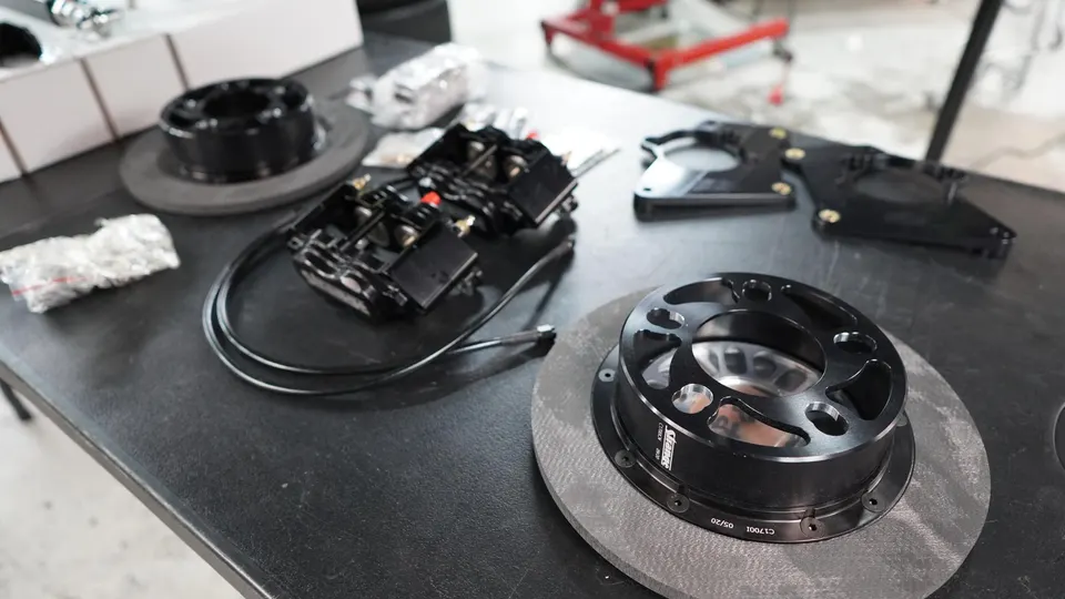 Performance brake kit components including rotors, calipers, and mounting hardware laid out on a table in a shop.