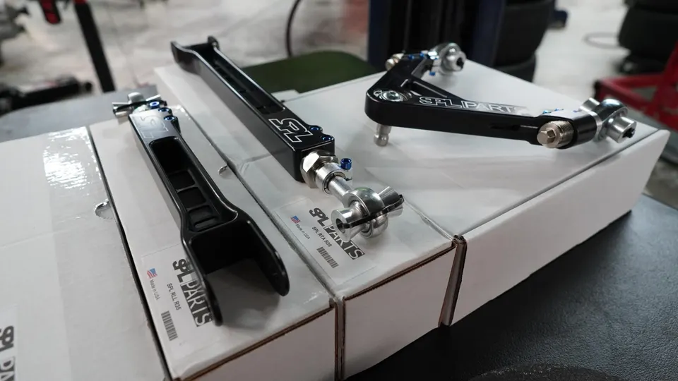 SPL Parts adjustable suspension components, including control arms, laid out on their packaging boxes.