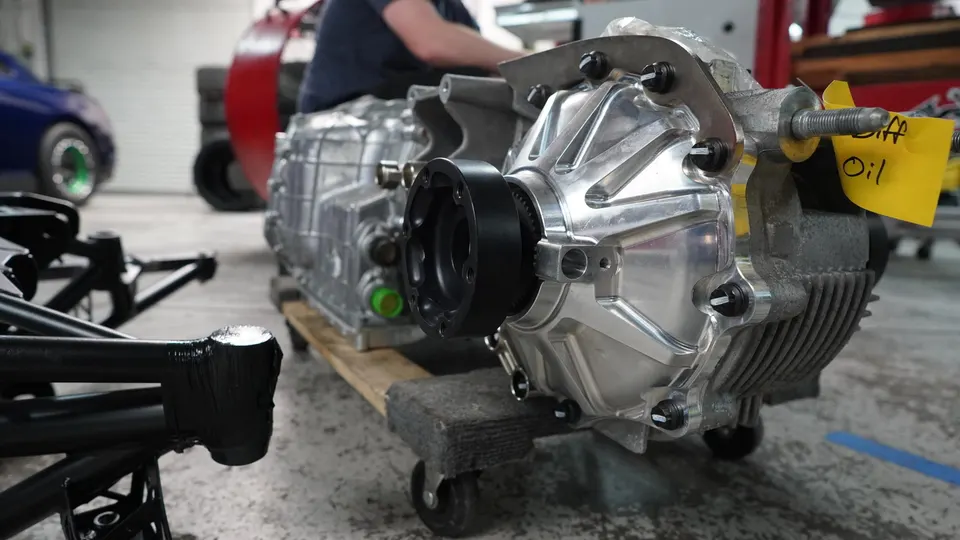 A close-up of a performance car transmission and differential assembly on a dolly in a workshop.
