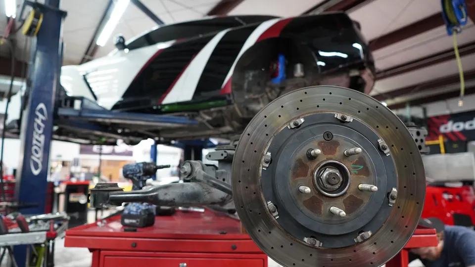 A Nissan GT-R on a lift in a performance shop with a brake rotor and hub assembly on a workbench in the foreground.