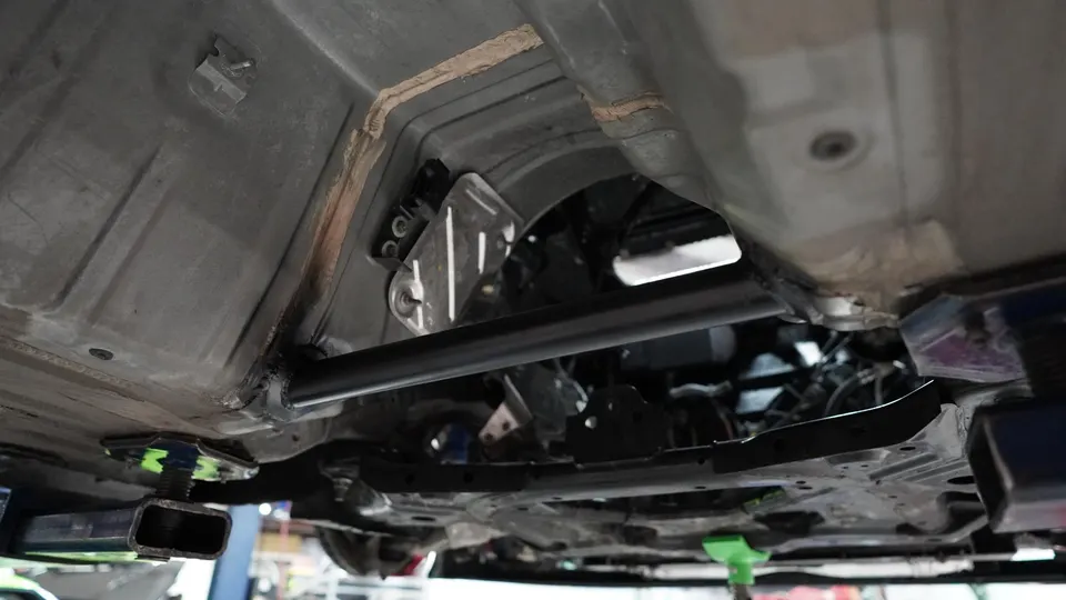 Underside view of a car on a lift in a performance shop, showing chassis and subframe brace.