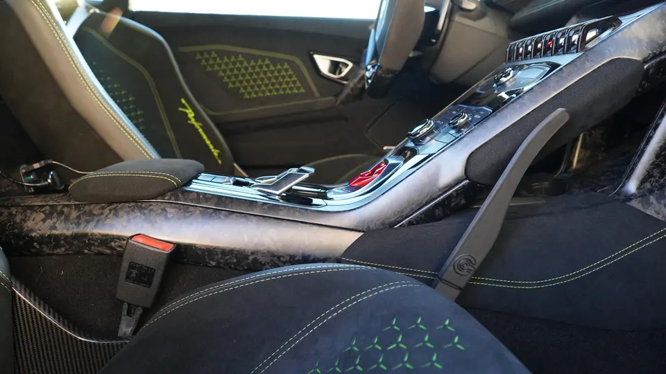 Detailed view of a Lamborghini interior featuring carbon fiber trim, black seats with lime green stitching, and the center console.