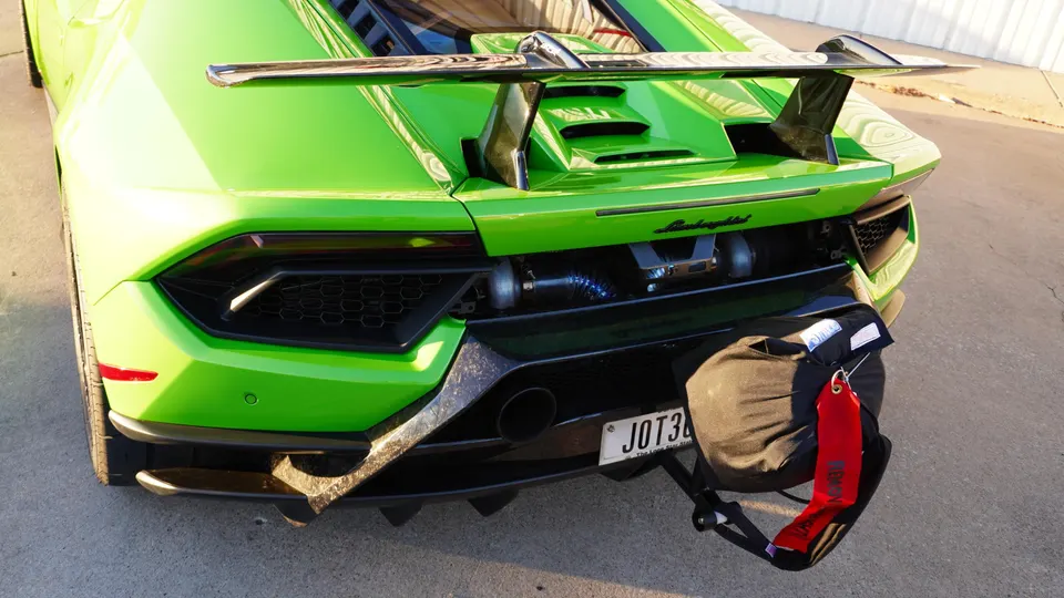 A bright green Lamborghini Huracan with a large rear wing and a drag parachute attached to the rear, parked on an asphalt surface.