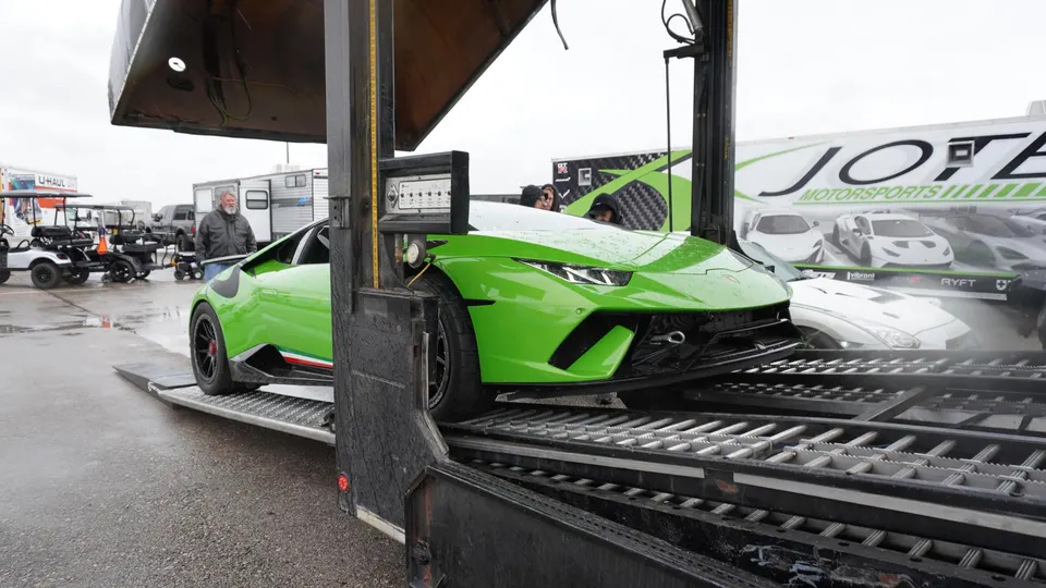 Green Lamborghini Huracan being unloaded from a car hauler at a track event, with Jotech Motorsports trailer in background.