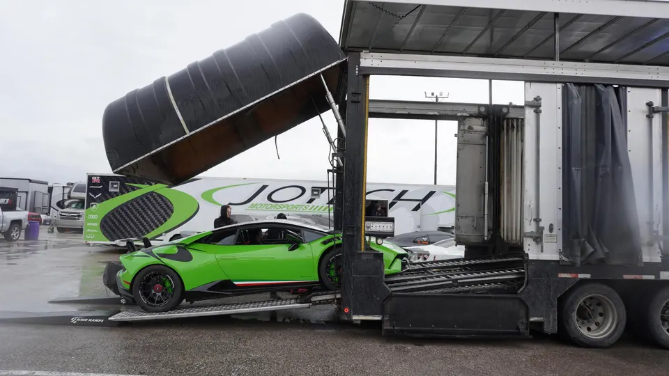 Green Lamborghini Huracan race car being unloaded from a Jotech Motorsports trailer at a track event.