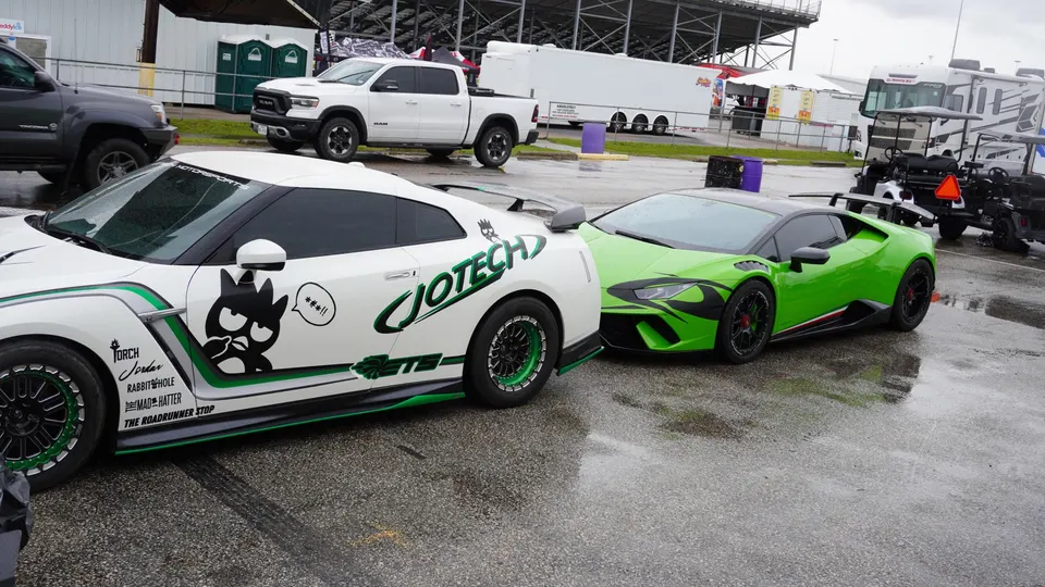 Two high-performance cars, a white Nissan GT-R with Jotech livery and a green Lamborghini Huracan, parked at a wet drag strip.