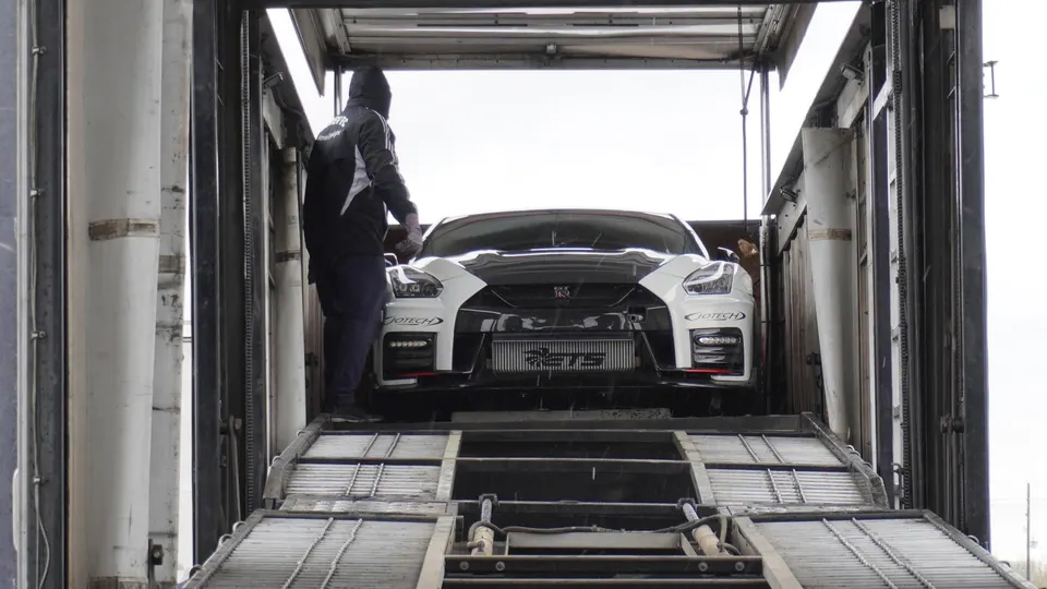 White Nissan GT-R with Jotech branding and large intercooler being unloaded from a car carrier.