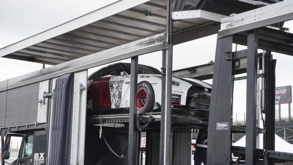 A highly modified white and red Nissan GT-R drag car being transported in a car hauler at a race track.