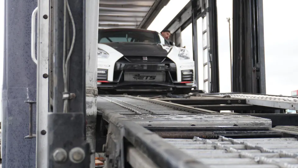 A white and black Nissan GT-R with an ETS intercooler being loaded onto a car carrier.