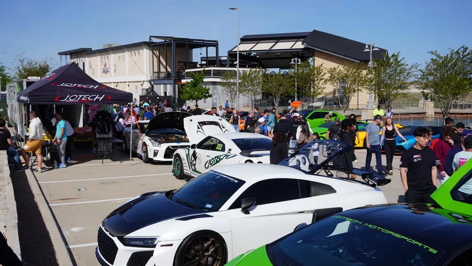 Jotech Motorsports tent at an outdoor car meet with modified Nissan GT-Rs, Audi R8, and Lamborghinis on display.