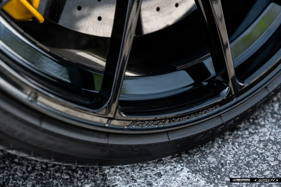 Close-up of a black multi-spoke wheel with a yellow brake caliper and drilled rotor on a performance car.