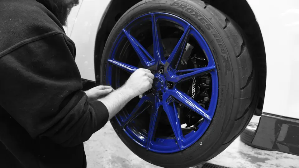 A person working on a car's blue aftermarket wheel and tire in a shop setting.