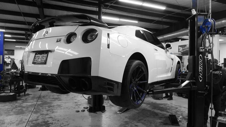 A white Nissan GT-R on a car lift in a performance tuning shop, viewed from the rear.