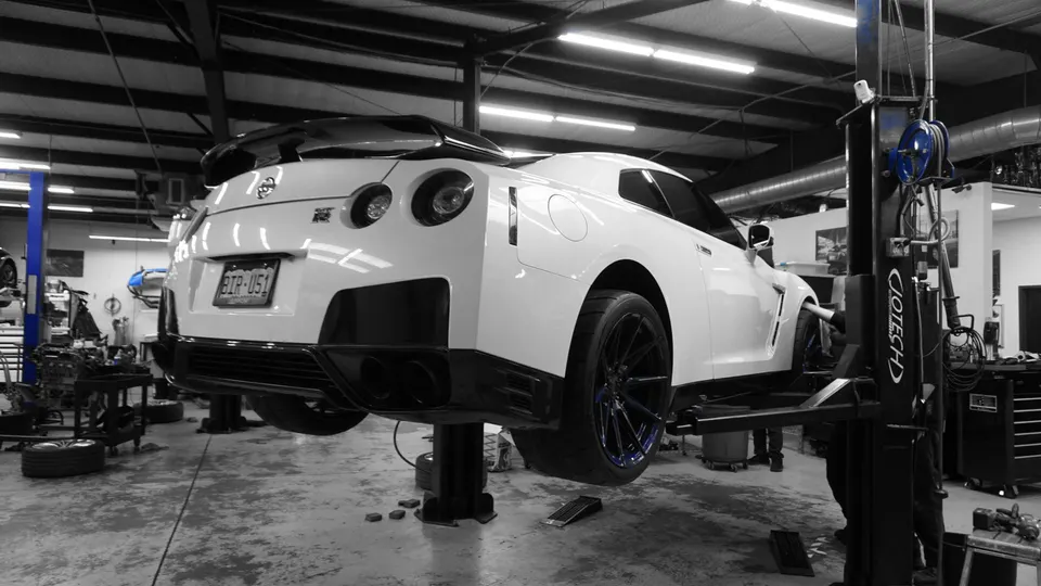 A white Nissan GT-R on a car lift in a workshop, showing the rear and side of the vehicle.